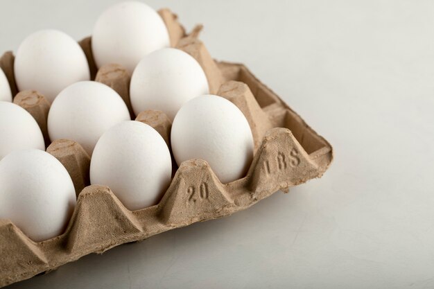 Raw chicken eggs in egg box on a white surface. 