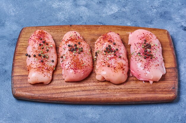 Raw chicken fillet on a wooden board on blue