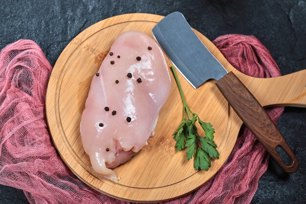 Raw chicken fillet on wooden board with greens and knife.