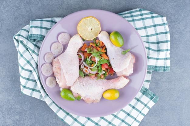 Free photo raw chicken legs with vegetables on purple plate.