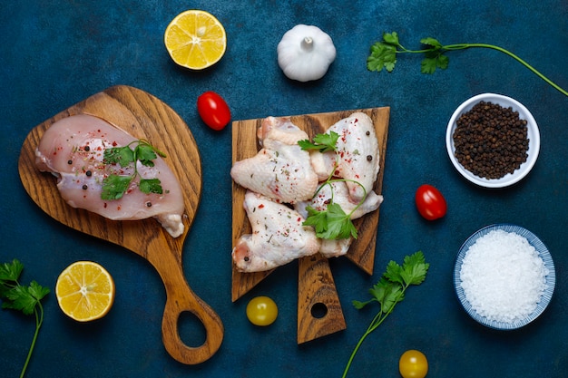 Free photo raw chicken meat fillet, thigh, wings and legs with herbs ,spices,lemon and garlic on dark blue background. top view