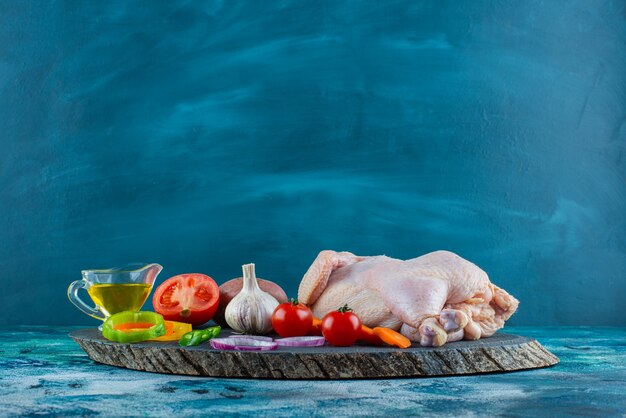 Raw chicken, vegetables and oil on a board on the blue surface