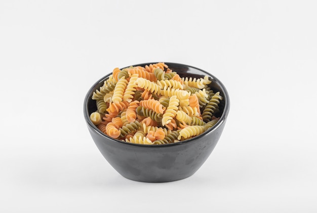 Raw colorful fusilli pasta in dark bowl.