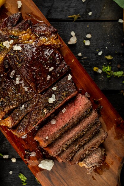 Raw cooked meat steak sliced and salt added, served on the black table