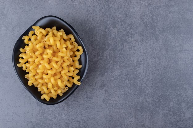 Raw dry macaroni in black bowl.