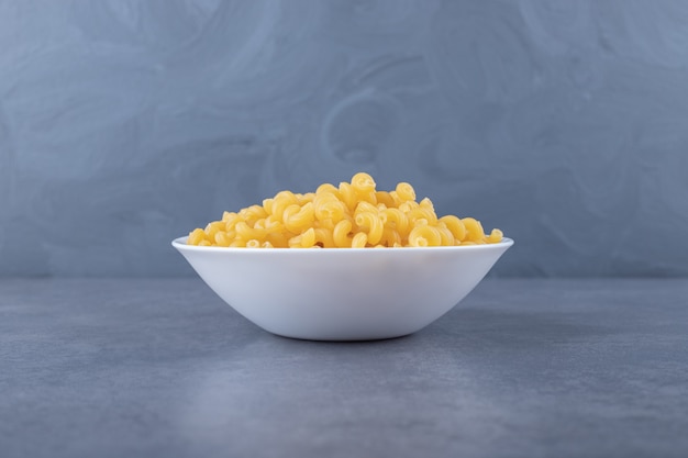 Raw elbow macaroni on white plate.