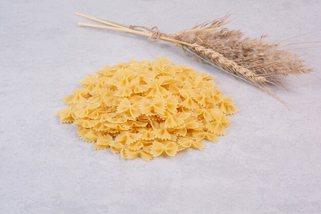 Raw farfalle pasta on white surface with wheat