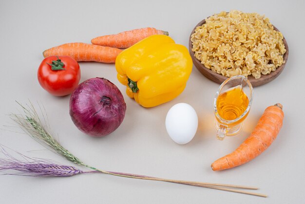 Raw macaroni with vegetables and egg on white surface