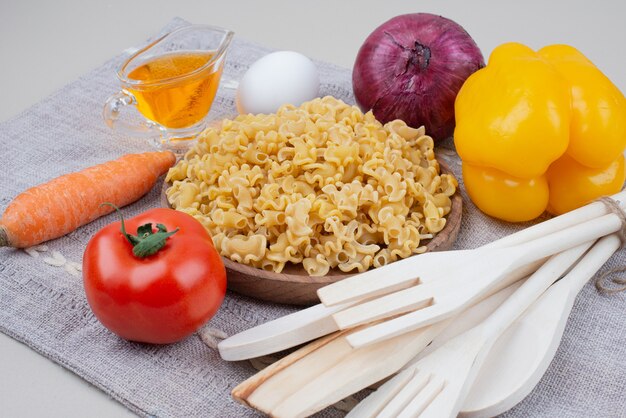 Raw macaroni with vegetables on wooden plate on tablecloth