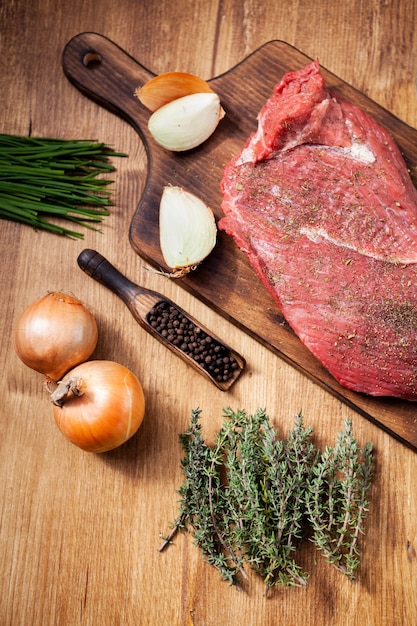 Free photo raw meat from the butcher shop on wooden board with ingredients. raw onions. green herbs.