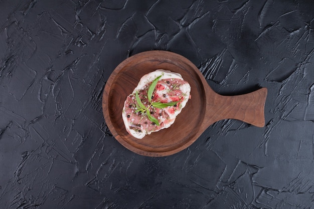 Free Photo raw meat piece on wooden plate decorated with fresh mint on dark background.