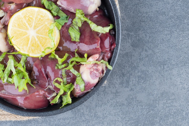 Raw meat slices and sliced lemon on black plate.