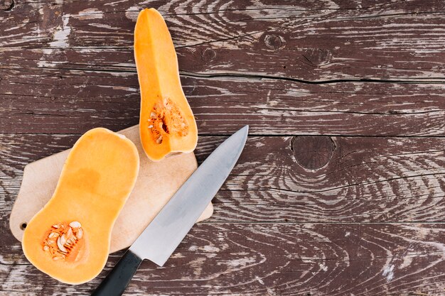 Raw orange organic butternut squash on chopping board with knife over the wooden desk