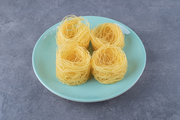 Free photo raw pasta nests on blue plate.