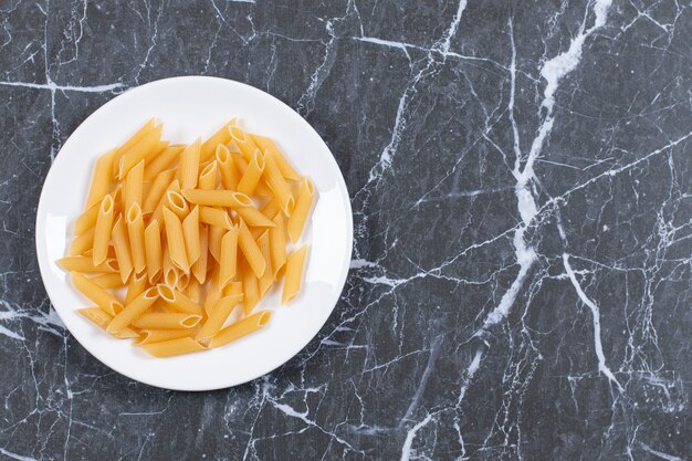 Raw pasta penne on white plate. top view.