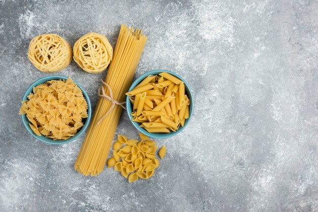 Raw pasta and spaghetti varieties on marble table.