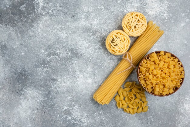 Raw pasta and spaghetti varieties on marble table.