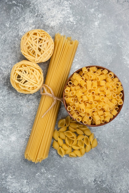 Raw pasta and spaghetti varieties on marble table.