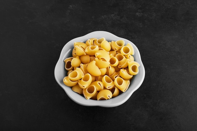 Raw pasta varieties in ceramic cup on black.