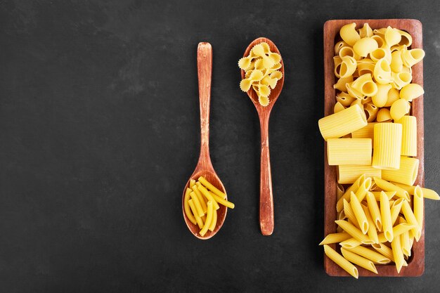 Raw pasta varieties on a wooden platter, top view.