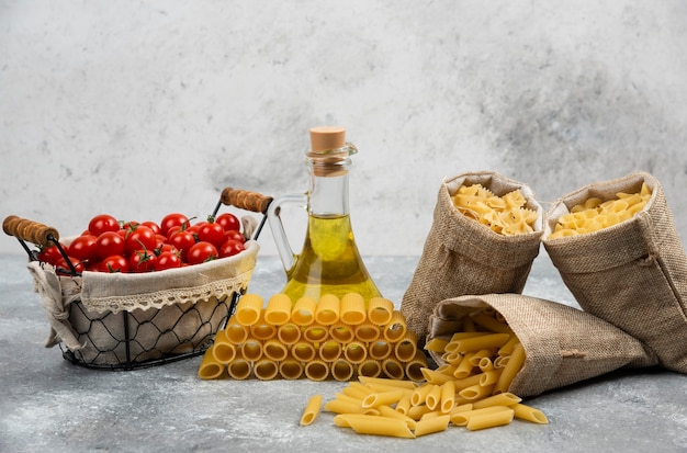 Raw pasta with a basket of cherry tomatoes and a bottle of olive oil.