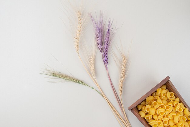 Raw pasta on wooden plate with colorful ears of wheat