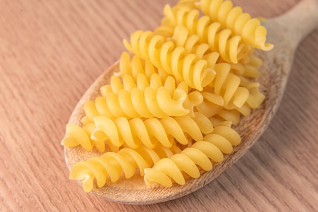 Raw pasta in wooden spoon on wooden table