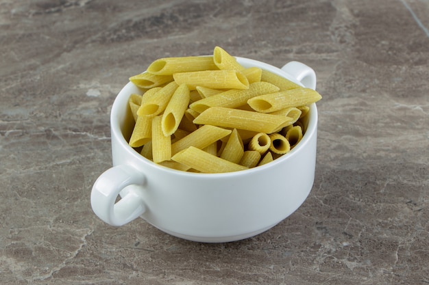 Raw penne pasta in white mug