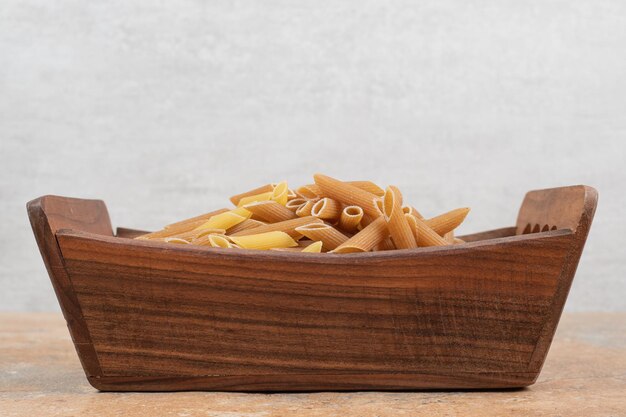 Raw penne pasta in wooden basket. 