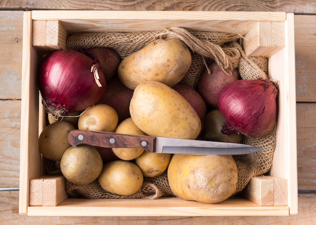 Free photo raw potatoes in wooden box with knife