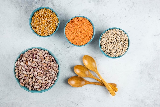 Raw red lentils, corns and beans in blue bowls with wooden spoons.