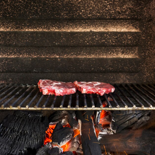 Raw red meat on grill pit with hot charcoal briquettes