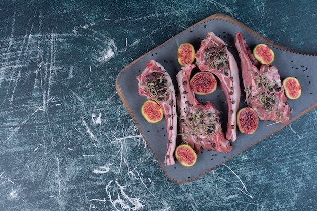 Raw rib chops in wooden board with figs and dried herbs.