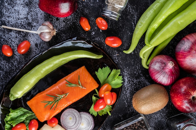 Free photo raw salmon fillets, pepper, kiwi, pineapples, and rosemary onto a plate and black cement floor.