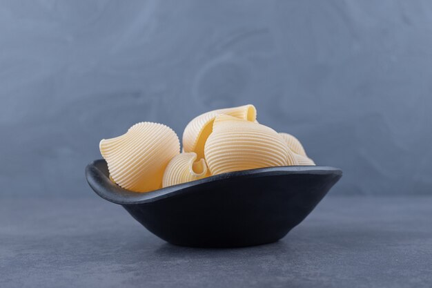 Raw seashell pasta in black bowl.