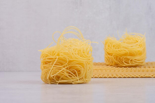 Raw spaghetti nests and pasta on marble table.