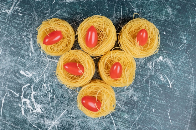 Free Photo raw spaghetti nests and tomatoes on blue background. high quality photo