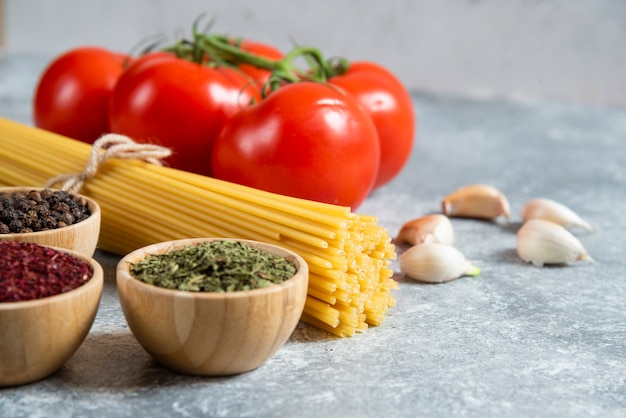 Raw spaghetti, spices and tomatoes on marble background.