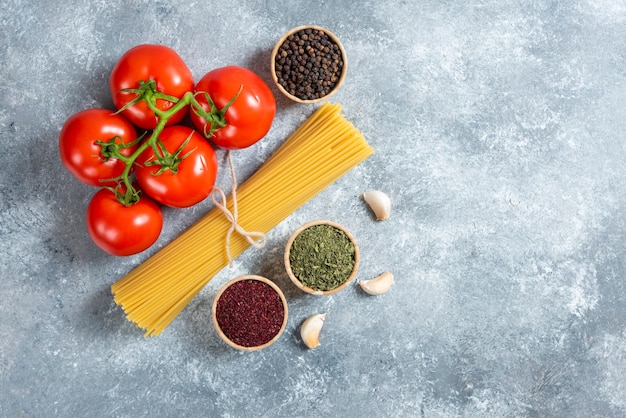 Free photo raw spaghetti, spices and tomatoes on marble background.