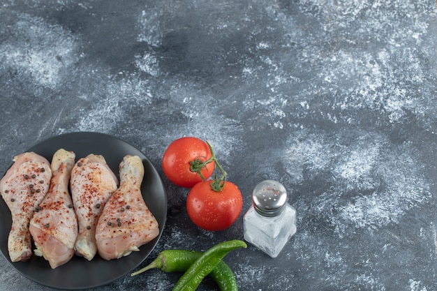 Free photo raw spicy chicken drumstick with tomato, pepper and salt on grey background.