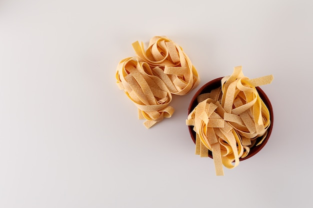 raw tagliatelle pasta in the bowl top view on white surface