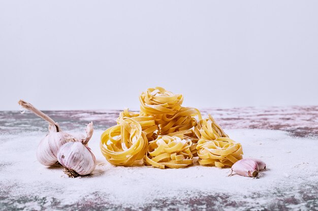 Raw tagliatelle with garlic on grey surface. 