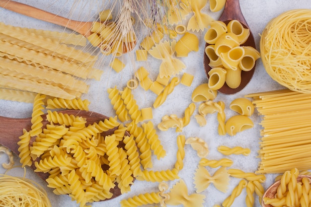 Raw various pasta shapes and spoons on white space. 