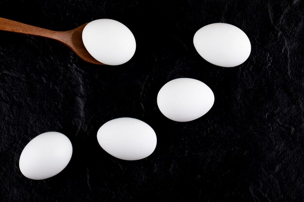 Raw white eggs and wooden spoon on black surface. 