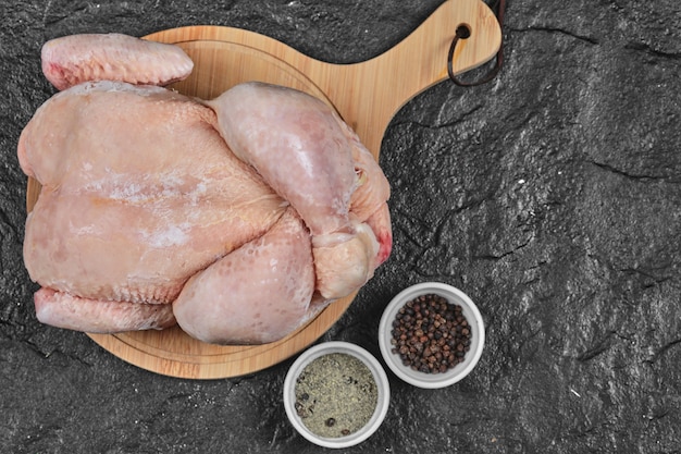 Raw whole chicken on wooden board with spices