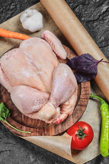 Free photo raw whole chicken on wooden plate with fresh vegetables