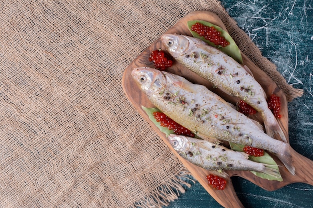 Raw whole fishes with red caviar on wooden board. 