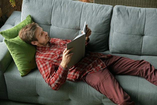 Reading book on sofa. Caucasian man staying at home during quarantine