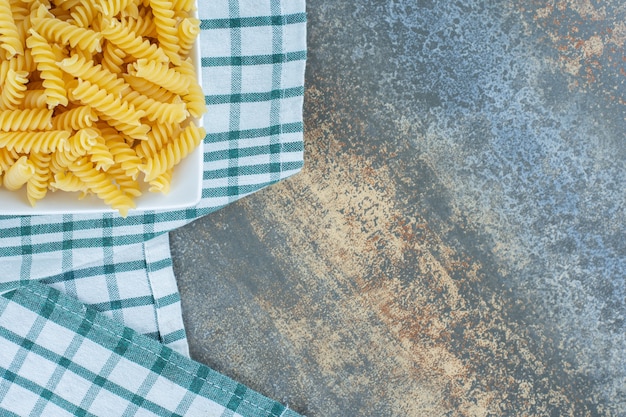 Ready to cook fusilli pasta in bowl on towel, on the marble surface. 