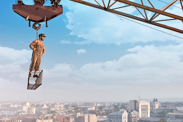 Free photo ready for the day. low angle portrait of a young muscular retro builder posing on a crossbar hanging from a crane on a skyscraper